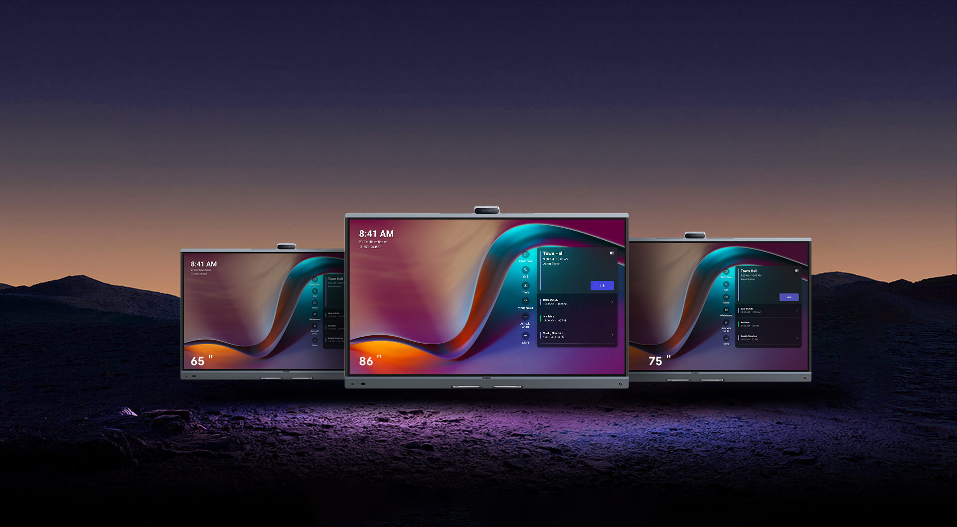 Three flat-screen smart TVs of different sizes are displayed side by side on a dark surface with a colorful interface on their screens against a dusk sky background.