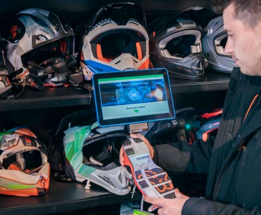 A person scanning a product using a barcode scanner connected to a tablet in front of shelves with helmets.