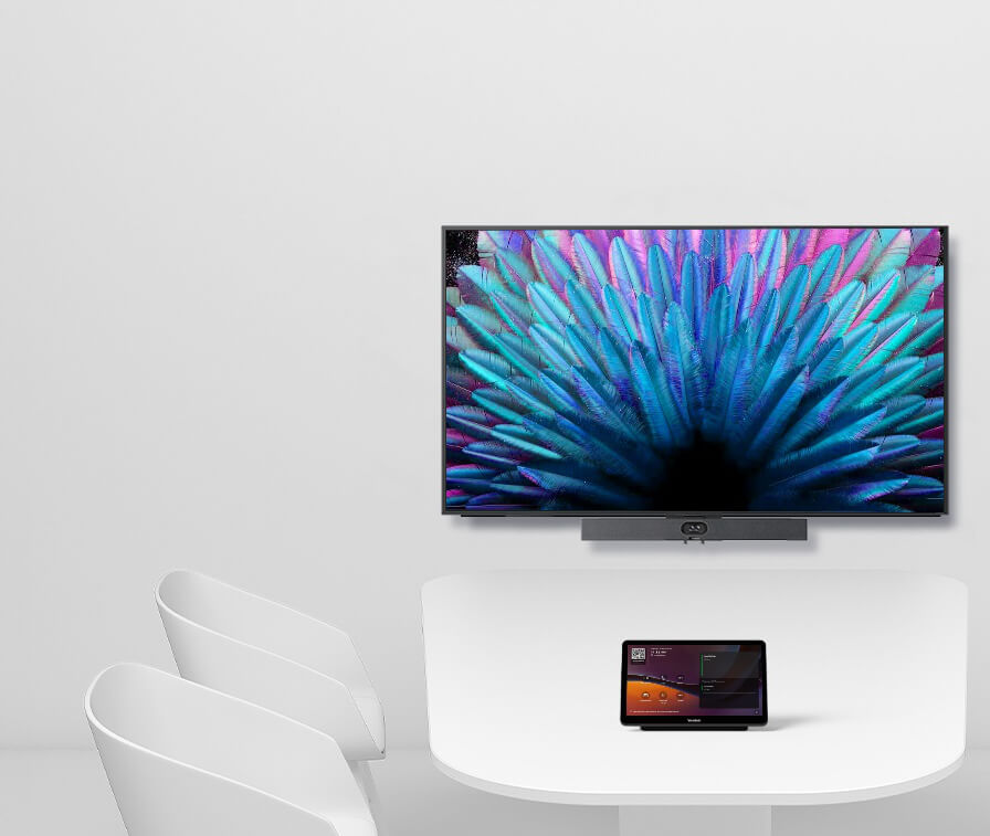 A white table with a tablet on it is positioned in front of two white chairs; a wall-mounted television displays a colorful abstract image in the background.