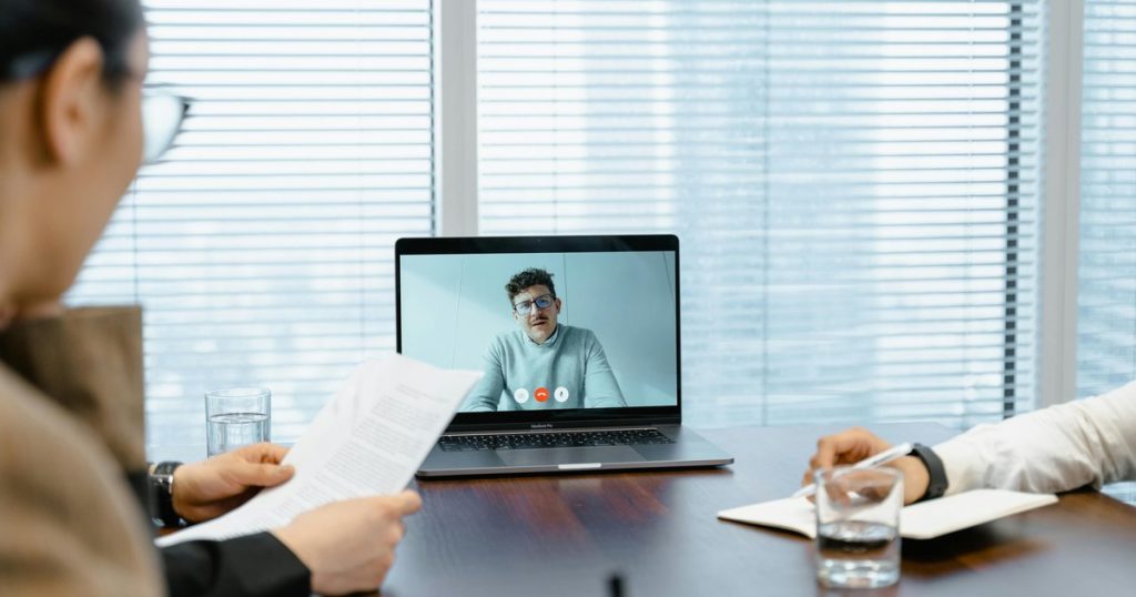 Diverse team participating in a hybrid video conference meeting with remote participant on screen in a modern corporate meeting room